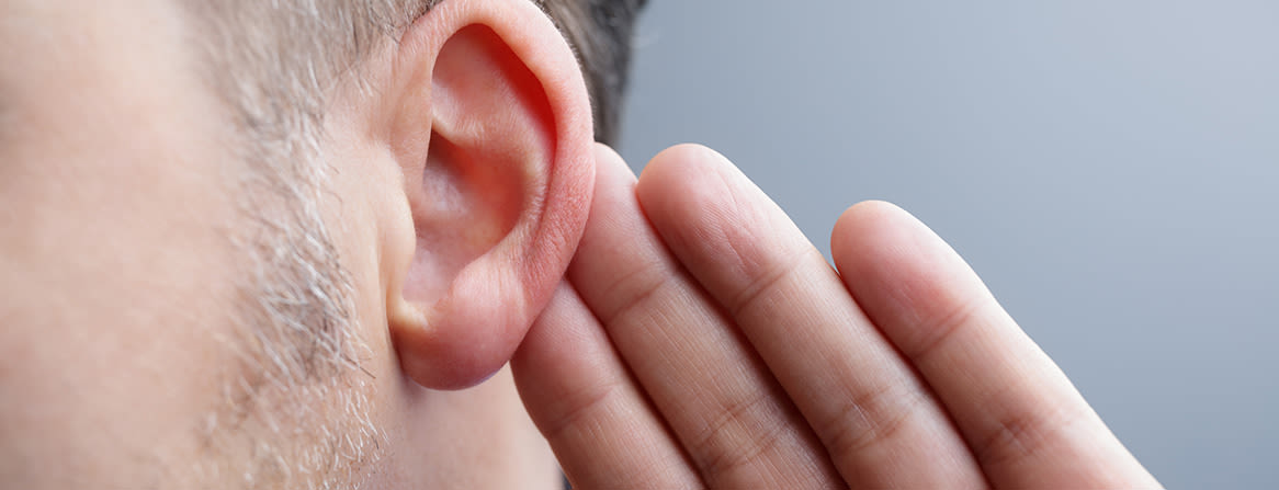 Mies kuuntelee tarkasti käsi korvan vieressä.