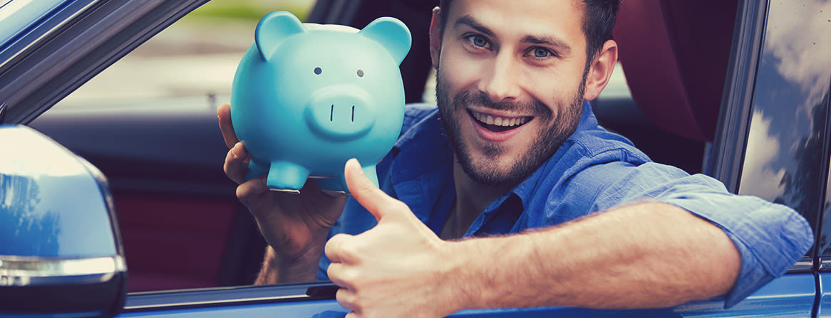 Hymyilevä mies autossa pitää sinistä säästöpossua ja näyttää peukkua.