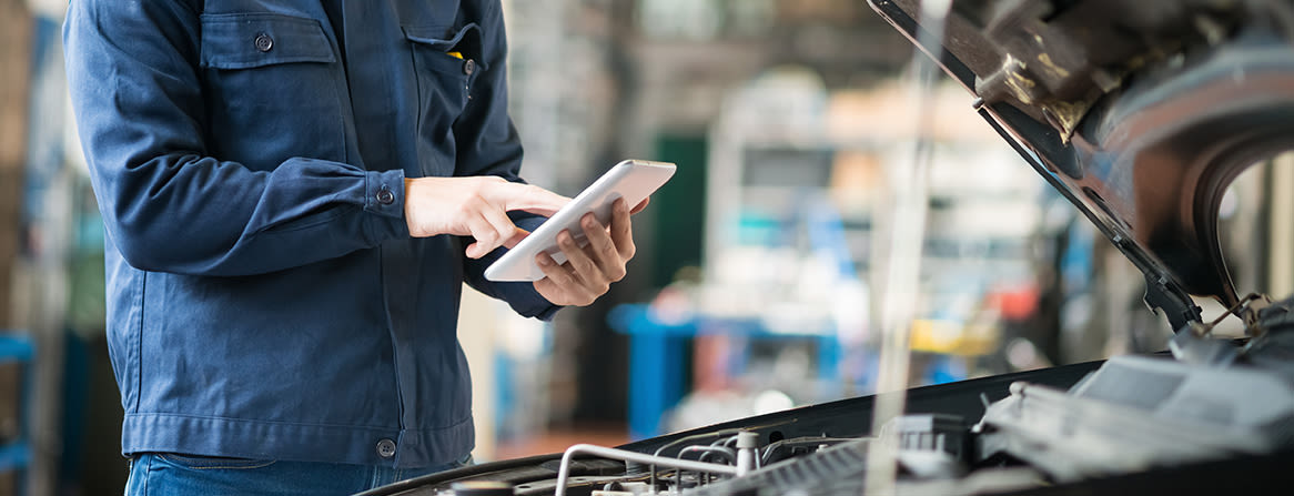 Mekaanikko käyttää tablettia avoimen konepellin äärellä.